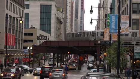 Chicago-CTA-loop-train-riding-on-elevated-railway-with-morning-traffic-beneath-on-a-cloudy-morning-in-downtown,-4K-slow-motion