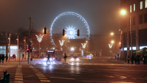 People-crossing-Street-at-night,-illuminated-Budapest-Eye-in-background