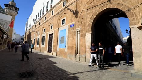 Los-Peatones-Tunecinos-Caminan-Por-Una-Calle-Adoquinada-Con-Una-Entrada-Arqueada