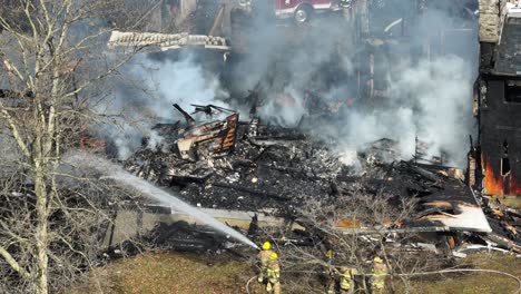 Firemen-with-yellow-protection-clothes,-spraying-water-on-burning-house