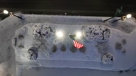 American-flag-waving-above-snowy-landscape-in-USA-town-at-night