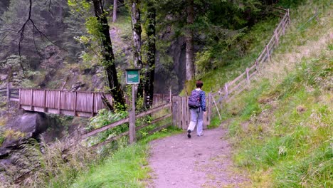 Woman-hiking-on-the-trail-to-the-Stieber-Waterfall-passing-trough-the-wooden-gate,-Moos-in-Passeier-Moso-in-Passiria,-South-Tyrol,-Italy