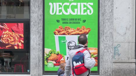 Fußgänger-Gehen-An-Einer-Straßenwerbung-Von-KFC-Vorbei,-Die-Ein-Neues-Vegetarisches-Gericht-Namens-Veggies-Vorstellt,-Das-In-Den-Fast-Food-Ketten-In-Spanien-Erhältlich-Ist