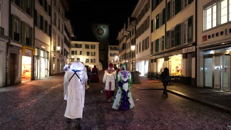 People-in-white-ghost-costume-walking-on-swiss-street-at-night-during-carnival