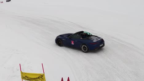 Drone-follow-dark-blue-convertible-car-drive-sideways-on-snowy-race-track