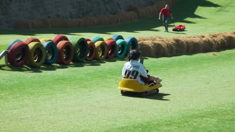 Young-Girl-Rides-Cart-Down-Grassy-Hill-And-Shooting-Phone-Video-at-Mongo-Land-Park,-Dalat,-Vietnam---slow-motion