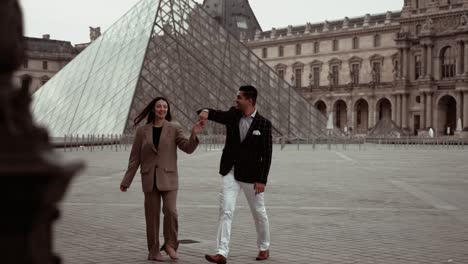 Elegant-couple-turning-a-pirouette-at-Museum-du-Louvre-Pyramid-surrounded-by-the-baroque-royal-residence-buildings-in-Paris-France-without-tourists---modern-lifestyle-and-suits-dating-lovers