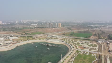 Rajkot-Atal-lake-drone-view-drone-camera-going-down-where-big-ashoka-chakra-and-lots-of-gardens-around-and-lots-of-big-buildings-around,-Rajkot-New-Race-Course,-Atal-Sarovar