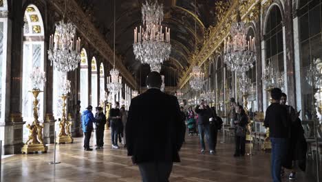 Männlicher-Tourist,-Der-Durch-Den-Berühmten-Historischen-Spiegelsaal-Im-Barockschloss-Versailles,-Paris,-Frankreich,-Mit-Vielen-Kronleuchtern,-Gemälden-Und-Goldenen-Ornamenten-Geht