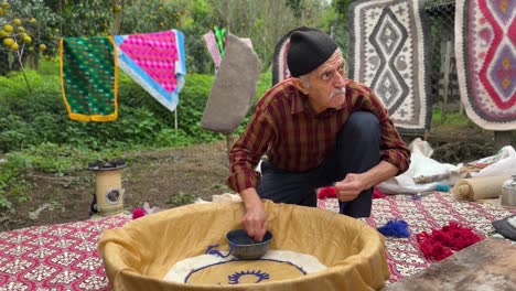 old-artist-man-wear-wool-headwear-design-handmade-rug-Persian-carpet-namad-the-felt-beating-woolen-fiber-made-sheep-wool-carpet-traditional-process-of-beating-rolling-and-pressing-fabric-to-compress