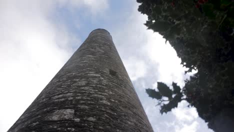 An-establishing-reveal-shot-looking-up-at-the-tall-Round-Tower-at-Glendalough,-an-ancient-historical-landmark-in-Wicklow,-Ireland