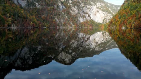 Crystal-clear-lake-reflects-vibrant-mountain-peaks,-sunlight-dances-on-glassy-surface