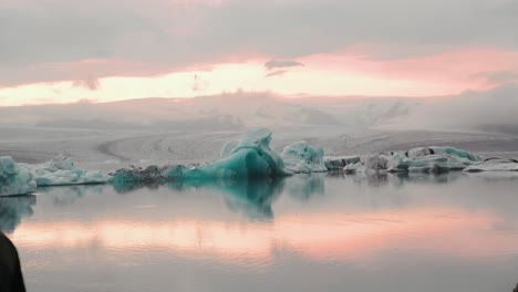 Iceberg-swimming-in-Jokulsarlon,-Iceland-in-glacier-lagoon-during-golden-hour-sunset,-reflections-in-water