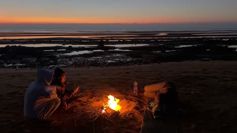 Camping-Costero-Cerca-De-La-Playa-Maravilloso-Amanecer-Sobre-El-Horizonte-Horizonte-Con-Luces-De-Colores-Vivos-Gente-Reunida-Alrededor-Del-Fuego-Viaje-Alegre-Y-Pacífico-A-Qeshm-Saborea-La-Cultura-árabe