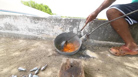 Man-casting-molten-lead-in-a-mold-outdoors-with-ladle,-traditional-metalworking-process,-sunny-day