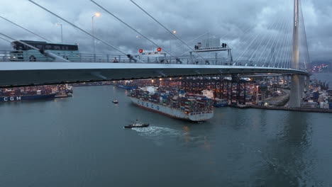 Fahrzeuge-Auf-Einer-Hängebrücke-Mit-Einem-Containerschiff,-Das-Sich-An-Einem-Bewölkten-Tag-Dem-Hafen-Nähert