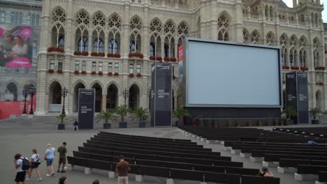 Menschen-Gehen-In-Der-Nähe-Des-Wiener-Rathauses-Spazieren,-Im-Hintergrund-Ist-Eine-Riesige-Leinwand-Zu-Sehen