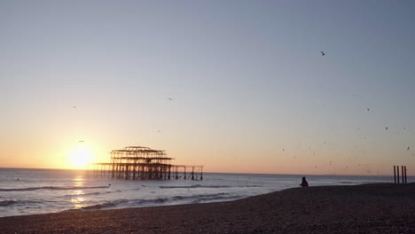 Wide-Shot-of-Silhouetted-West-Pier,-Brighton-at-Sunset-with-Birds-Flying