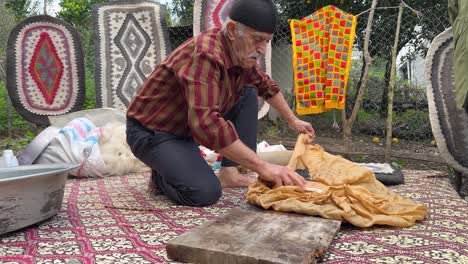 old-man-rolling-handmade-rug-the-woolen-fiber-material-to-make-natural-traditional-carpet-the-soft-touch-mat-made-by-pressing-rolling-designed-pattern-in-local-rural-village-countryside-in-Iran