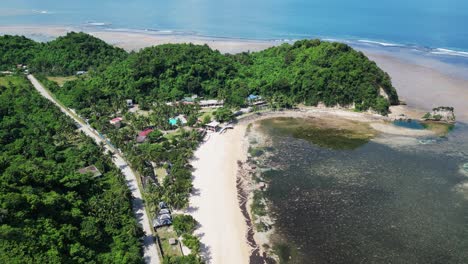 Aerial-forward-drone-shot-of-tropical-white-sand-beach-resort-with-lush-hills-and-shallow-reef-during-low-tide