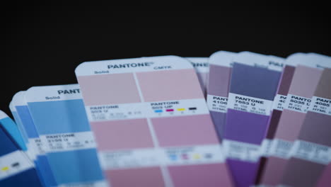 Pantone-color-fan-guide-of-media-agency-for-determination-of-printing-in-front-of-black-background,-slow-camera-pan