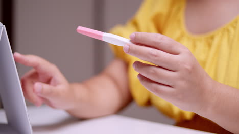 Holding-the-result-of-her-pregnancy-test-using-a-test-kit,-the-pregnant-woman-is-counting-the-weeks-to-her-expected-due-date-using-a-calendar