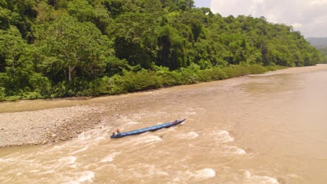 Long-canoe-navigated-by-local-on-the-muddy-waters-of-Oxapampa-river,-surrounded-by-dense-jungle