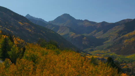 Colorado-summer-fall-autumn-colors-aerial-drone-cinematic-Aspen-Snowmass-Mountain-Maroon-Bells-Pyramid-Peak-beautiful-stunning-blue-sky-mid-day-sunny-reveal-past-yellow-trees-upward-movement