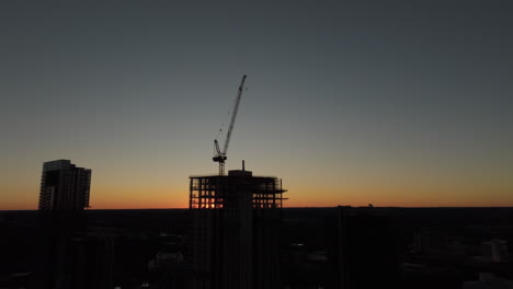 Aerial-shot-of-silhouette-of-crane-building-apartments-and-offices-on-a-construction-site-at-sunset