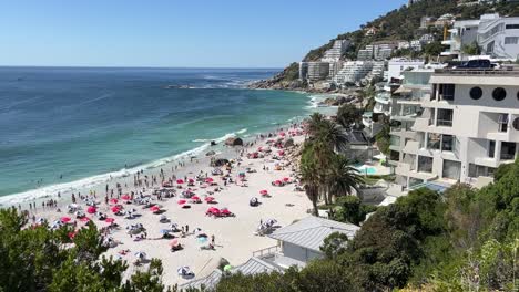 Un-Alto-ángulo-De-Vista-De-Una-Concurrida-Playa-De-Clifton-Y-Hoteles-En-Ciudad-Del-Cabo,-Sudáfrica,-Nadadores-Y-Bañistas-Empacan-La-Playa-Y-Entran-Olas