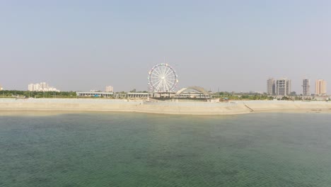 Vista-De-Drones-Del-Lago-Rajkot-Atal,-Muchas-Aves-Vuelan-En-La-Cámara-De-Drones-Y-También-Se-Ve-El-Gran-Lago-Y-La-Gran-Rueda-Gigante,-El-Nuevo-Hipódromo-De-Rajkot,-Atal-Sarovar