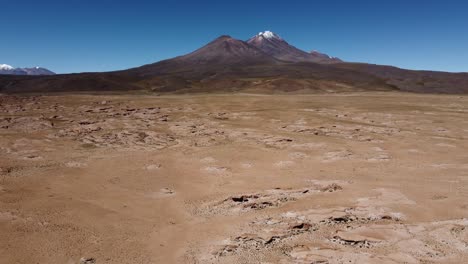 Flyover-volcanic-fumaroles-toward-distant-snow-peak-mountain,-Bolivia