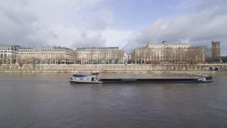 Wide-static-side-profile-footage-of-a-barge-slowly-moving-against-the-current-of-the-Seine-through-Paris-in-winter