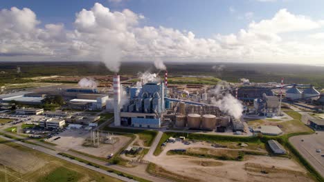 Aerial-orbit-over-a-big-industrial-plant-on-a-sunny-day---a-modern-cellulose-factory,-wide-shot-against-the-sun