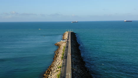 Aerial-view-of-footbridge-with-people-walking-around,-the-sea-and-two-boats-in-the-backgroud,-Fortaleza,-Ceara,-Brazil
