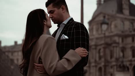 Lovely-elegant-couple-in-suits-holding-each-other-close-with-closed-eyes-feeling-the-deep-moment-of-love-the-Museum-du-Louve-surroundet-by-its-majestic-baroque-architecture-buildings-in-Paris-France