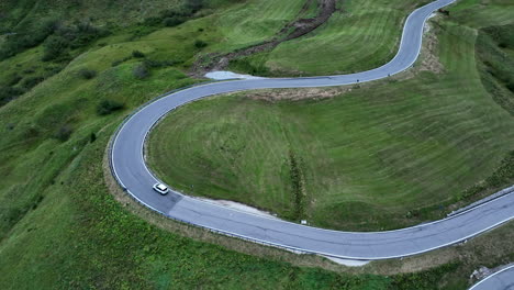Lonely-car-driving-on-winding-mountain-load-surrounded-with-green-meadows,-aerial-view