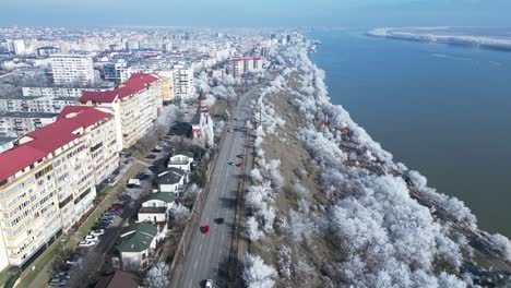 Recorrido-Panorámico-Por-Una-Carretera-Asfaltada-A-Través-Del-Paisaje-Urbano-Y-árboles-Invernales-Junto-Al-Río-Danubio