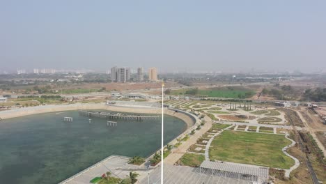 Vista-Desde-Drone-Del-Lago-Rajkot-Atal,-Todo-Se-Ve-Bien-Y-La-Cámara-Se-Mueve-Hacia-Abajo,-Se-Ven-Muchos-Autos-Grandes-Y-Muchos-Lagos-Grandes-Alrededor,-Nuevo-Circuito-De-Carreras-De-Rajkot,-Atal-Sarovar