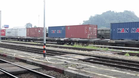 Toma-Panorámica-De-Vagones-De-Tren-Que-Transportan-Contenedores-De-Carga-Para-Compañías-Navieras-Estacionados-En-La-Estación-De-Tren-De-Thungsong-Junction