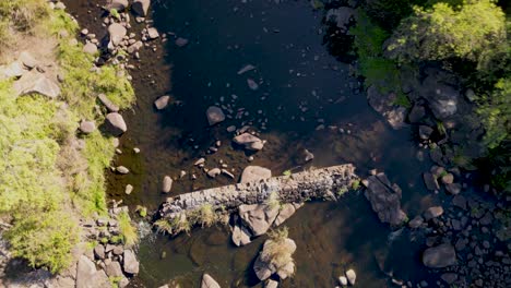 Drone-Vertical-Despega-Sobre-El-Río-Jandula-Sembrado-De-Rocas,-Paisaje-De-Andalucía