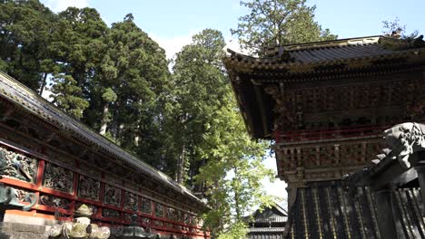 Ancient-Nikko-Toshogu-shrine-with-ornate-bell-tower-and-corridor,-lush-trees,-sunny
