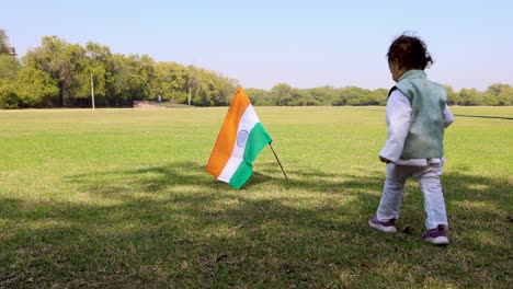 Kind-Geht-Zu-Fuß,-Um-Die-Indische-Trikolore-Nationalflagge-Zu-Halten,-Die-Tagsüber-Auf-Dem-Grünen-Spielplatz-Weht