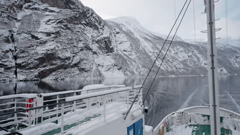 POV-video-of-a-ferry-ride-through-Geirangerfjord-in-winter,-featuring-stunning-views-of-snow-covered-mountains,-a-bright-sky,-and-reflections-in-the-fjord