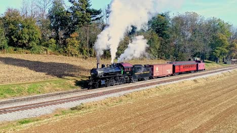 Eine-Luftaufnahme-Eines-Antiken-Güterzuges-Mit-Dampfantrieb,-Der-Rauch-Ausstößt,-Während-Er-An-Einem-Herbsttag-Langsam-Fährt