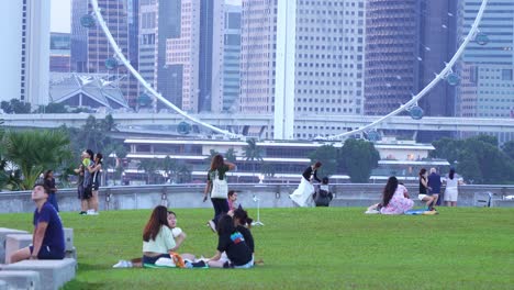 Marina-barrage-rooftop-urban-park-and-water-dam,-static-shot-capturing-people-picnic-and-hangout-on-the-green-grass-with-Singapore-Flyer-observation-wheel-and-downtown-cityscape-in-the-background