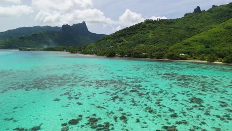 FPV-drone-flying-over-coral-reef-in-Moorea,-French-Polynesia-with-mountains-in-the-background