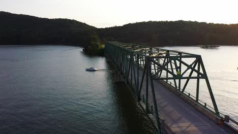 Motor-boat-passing-under-road-bridge-over-water-surface-at-sunset