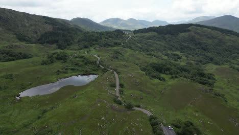 Aerial-shot-of-the-lush-Ladies-View-in-Ireland-with-a-winding-road-and-a-pond,-under-overcast-skies