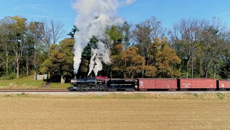 Eine-Luftaufnahme-Eines-Antiken-Güterzuges-Mit-Dampfantrieb,-Der-Rauch-Ausstößt,-Während-Er-An-Einem-Herbsttag-Langsam-Fährt